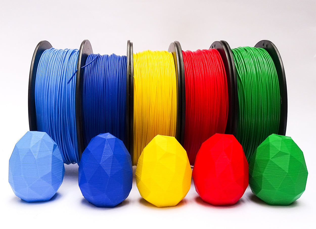 Rollos de Filamento PLA Print3x junto con huevos impresos en 3D de los colores celeste, azul, amarillo, rojo y verde | printex printec print3c
